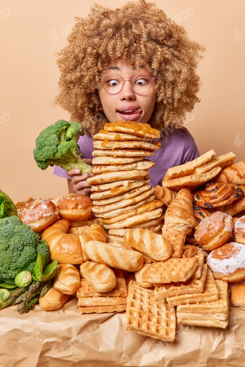 Preview: Photo of shocked woman with curly hair licks lips with tongue stares at appetizing sweet dessert