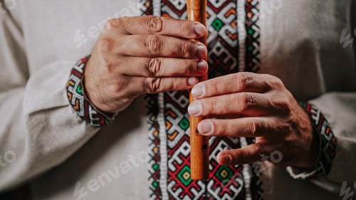 Preview: Hands of man playing on woodwind wooden flute - ukrainian sopilka on dark background.