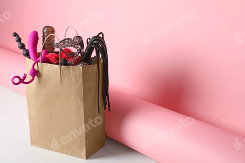 Preview: Paper shopping bag with different sex toys on pink background. Space for text