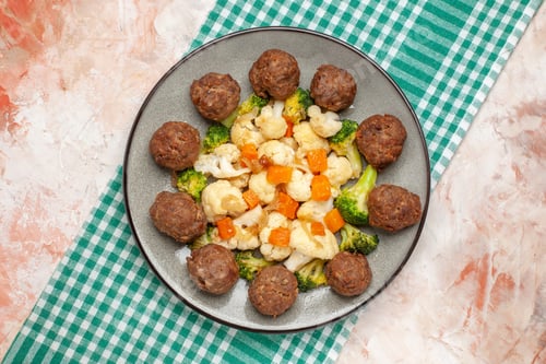 Preview: top view broccoli and cauliflower salad and meatball on plate green and white checkered napkin on