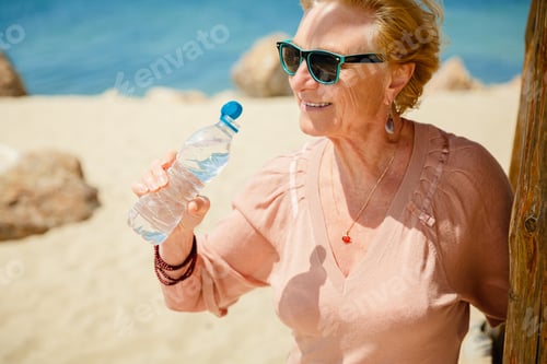 Preview: Senior woman sitting on the beach with a bottle of water