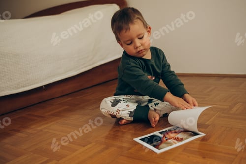 Preview: portrait of a child 2-3 years old sitting on the floor of the bedroom and looking at a photo album w
