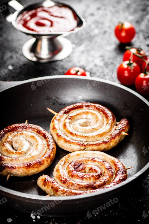 Preview: Delicious grilled sausages in a frying pan with fresh tomatoes.