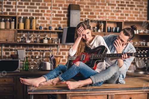 Preview: Young couple sitting on the kitchen table and holding guitar