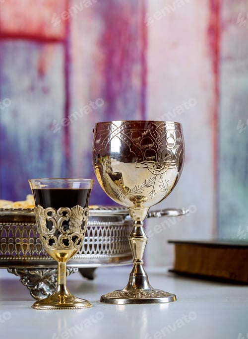 Preview: Taking Communion. Cup of glass with red wine, bread on wooden table close-up. Focus on wine