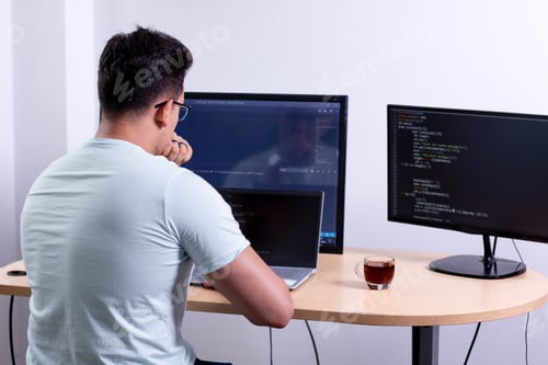Preview: Programmer analyzing his recently completed programming work with three monitors in his office.