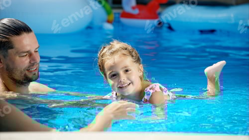 Preview: Little girl in sunglasses learning to swim in a pool with her father