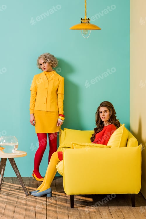 Preview: young retro styled women in colorful apartment with yellow sofa and aquarium fish, doll house