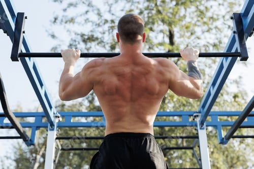 Preview: A muscular man pulls himself up on a horizontal bar in an outdoor park at sunset.