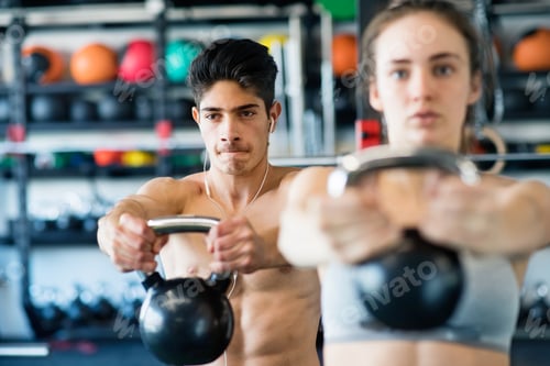 Preview: Young fit couple in gym exercising with kettlebell.