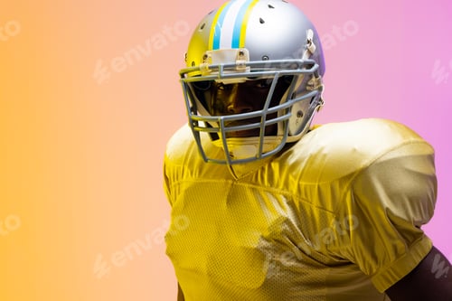 Preview: African american male american football player wearing helmet with neon yellow and purple lighting