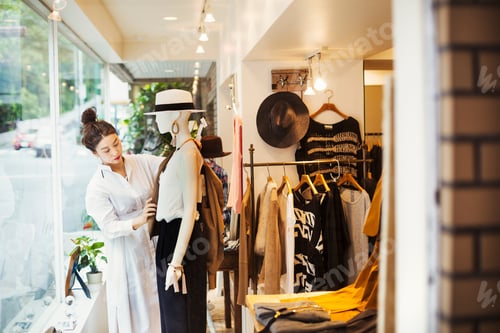 Preview: Woman working in a fashion boutique in Tokyo, Japan, dressing a mannequin.