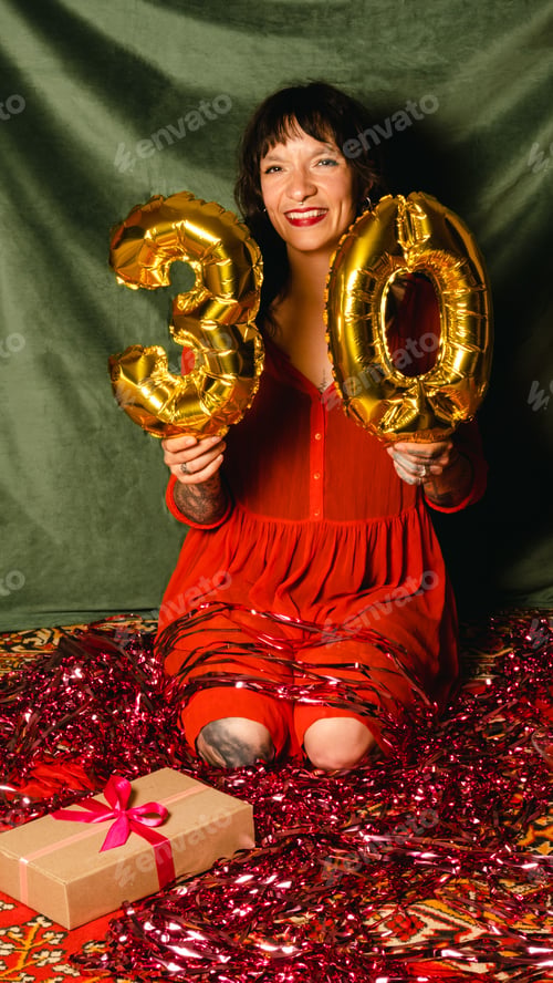 Vista previa: Young beautiful woman with piercings and tattoos holds balloons in the form of numbers 30.