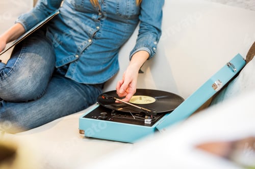 Preview: Cropped shot of young woman sitting on sofa listening to vintage record player