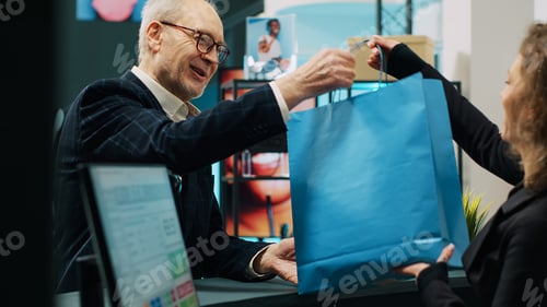 Preview: Checkout staff selling clothing items to senior customer in shopping mall