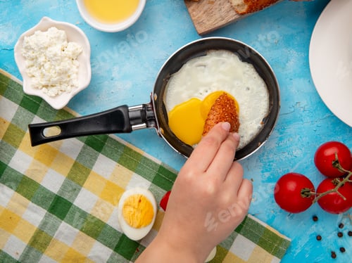 Preview: close-up view of woman hand eating fried egg with cottage cheese, tomato, black pepper on blue