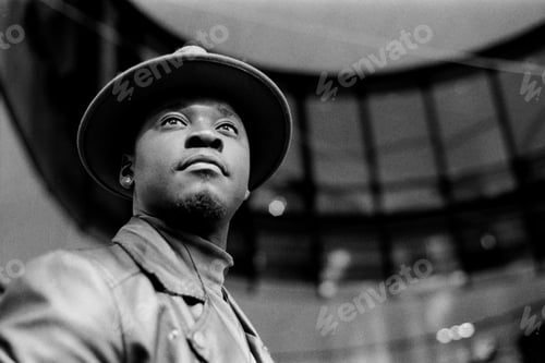 Preview: Authentic portrait of man wearing a hat and architectural background behind black and white image.