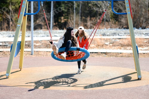 Preview: two teenager girls in caps on the playground. children's swing.