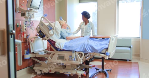 Preview: Female Doctor With Stethoscope Visiting Senior Female Patient In Hospital Bed Giving Her Good News