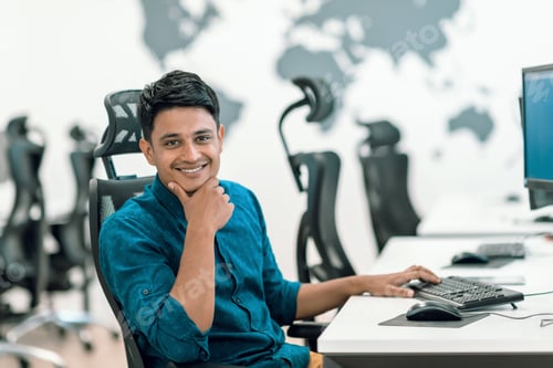 Preview: Casual business man working on desktop computer in modern open plan startup office interior.