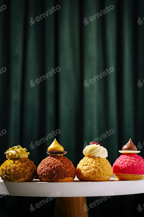 Preview: Four colorful pastries displayed on a table against a dark curtain backdrop
