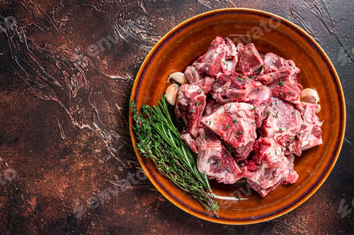 Preview: Raw mutton meat diced for goulash or stew with bone on a rustic plate. Dark background