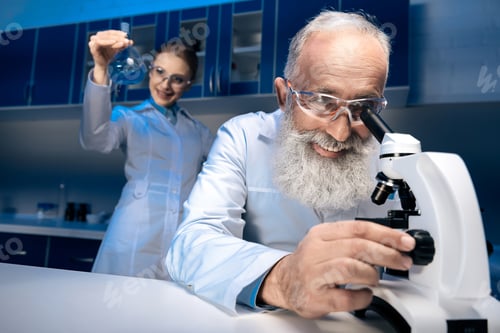 Preview: scientist using microscope while colleague holding reagent in tube in lab. scientists working