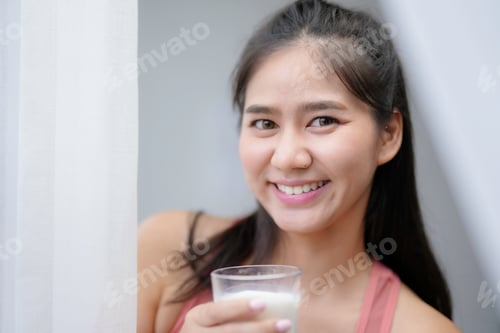 Preview: Young woman smiles happily while holding a glass of milk in her hands, embodying