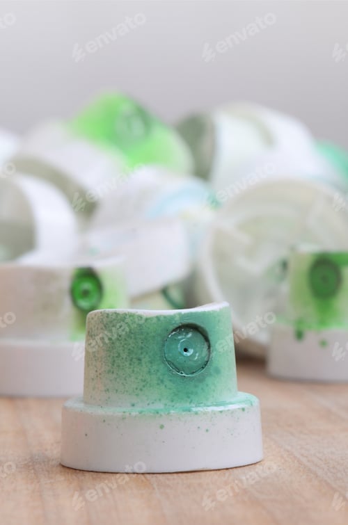 Preview: Several plastic nozzles from a paint sprayer that lie on a wooden surface against a gray wall