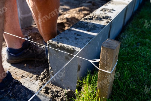 Preview: A man lays concrete blocks on a poured foundation, gluing them with mortar.