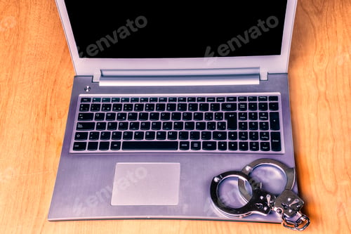 Preview: Silver laptop on the table with silver handcuffs. Cybersecurity concept.