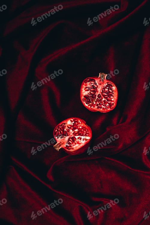 Preview: top view of ripe garnet halves on red velvet fabric background