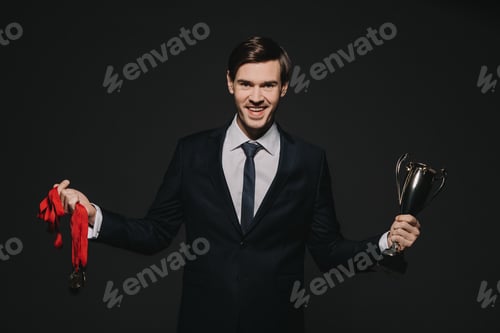 Preview: smiling businessman holding medals trophy in hands isolated on black