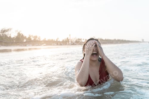 Preview: A young Hispanic woman is laughing playing with the waves in the sea at the beach