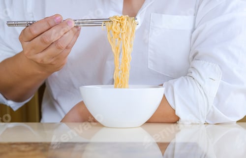 Preview: Close up man's hand in white shirt using silver chopsticks to eat instant noodles in white bowl