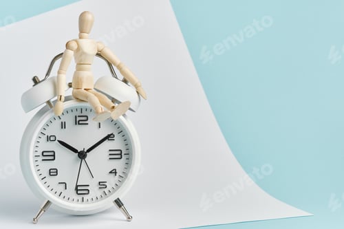 Preview: A wooden man sits on a white alarm clock. Time management, time control, punctuality.