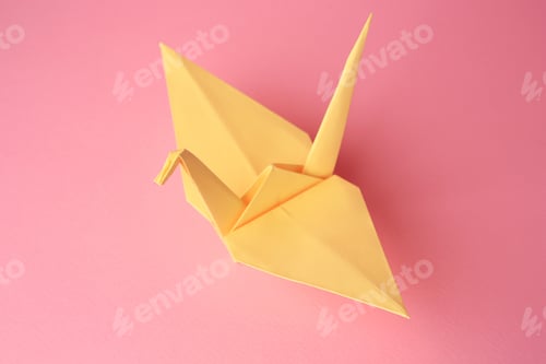 Preview: Origami art. Handmade paper crane on pink background, closeup