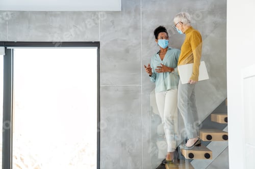 Preview: Businesswomen wearing masks collaborating in modern office, teamwork with laptop