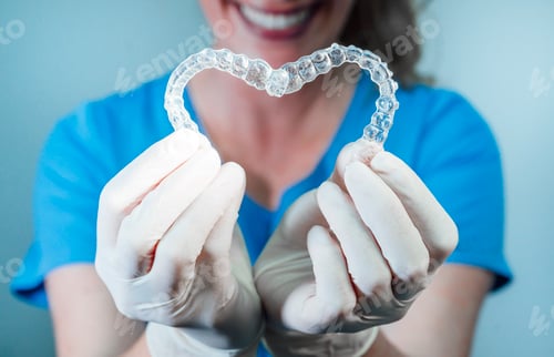Preview: Female doctor holding two transparent heart-shaped dental aligners