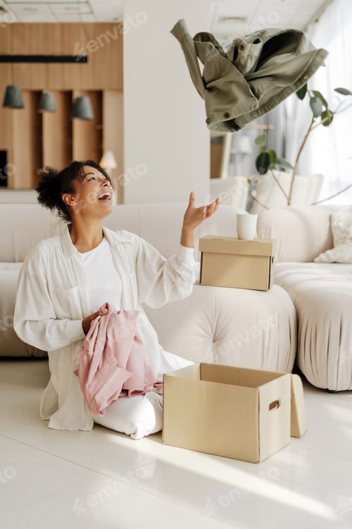 Preview: Woman having fun while packing clothes for donation in living room