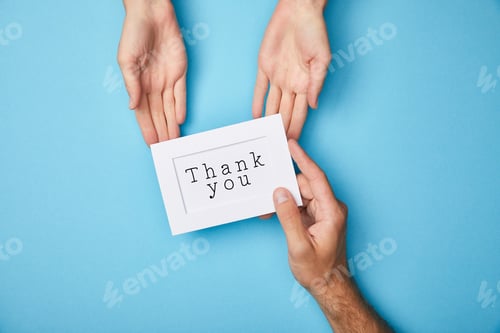 Preview: cropped view of man giving white card in frame with thank you lettering to woman on blue background