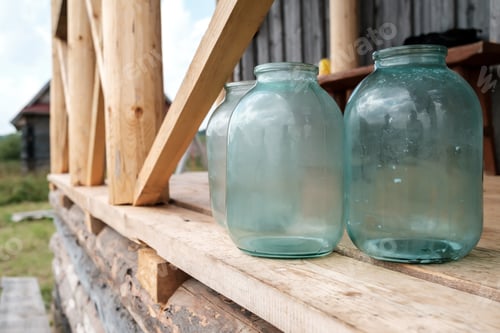Preview: Dirty glass jars standing on a wooden porch of a village house, in the yard