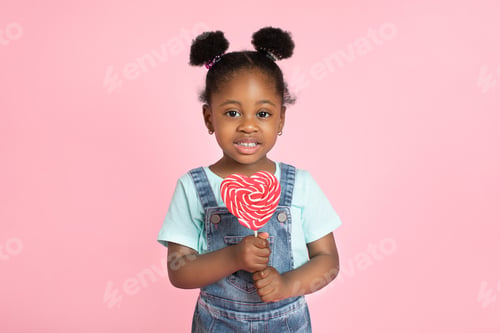 Preview: Close up portrait of adorable little African American black girl with red lollipop in heart shape