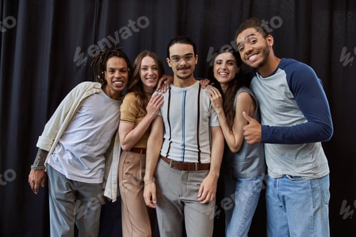 Preview: smiling african american man showing thumb up near multiethnic team in office on black backdrop