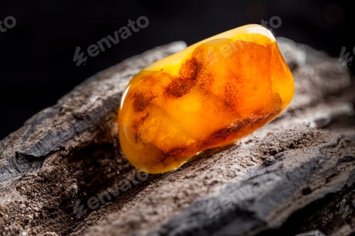 Preview: Natural amber. A piece of yellow opaque natural amber on large piece of dark stoned wood