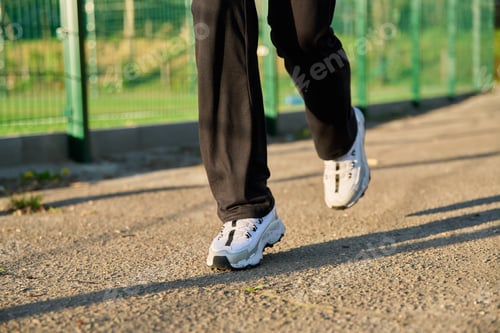 Preview: Close-up of female legs in white sneakers running along the road near the stadium