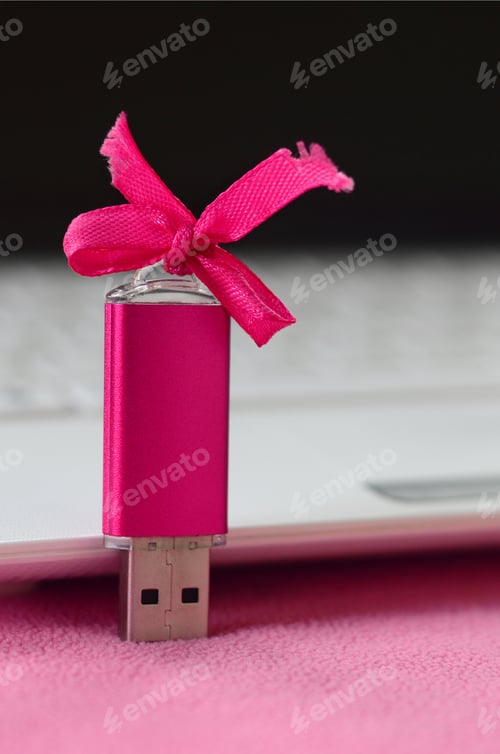 Preview: Brilliant pink usb flash memory card with a pink bow lies on a blanket
