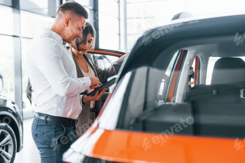 Vista previa: Documento informativo en mano. Hombre en ropa formal que ayuda al cliente con la elección del automóvil
