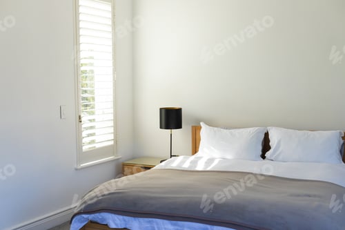 Preview: Bed with gray bedspread, white pillows and black lamp on nightstand in sunny bedroom