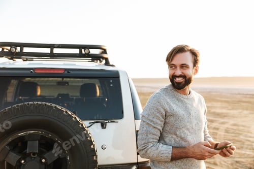 Preview: Man outdoors at the beach near car using mobile phone.